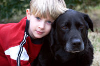 Blond boy hugging a black dog